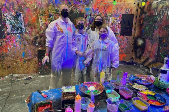 Family in protective suits and masks standing in a colorful art splatter room.